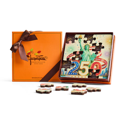 Jigsaw puzzle with Statue of Liberty design and chocolate pieces in front of an orange box with a bow.